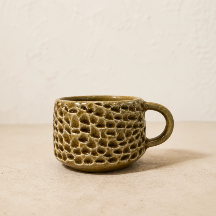 Close-up of a short rounded ceramic cup with glossy olive glaze and raised hand-carved pattern