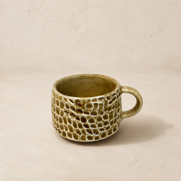 Close-up of a short rounded ceramic cup with glossy olive glaze and raised hand-carved pattern
