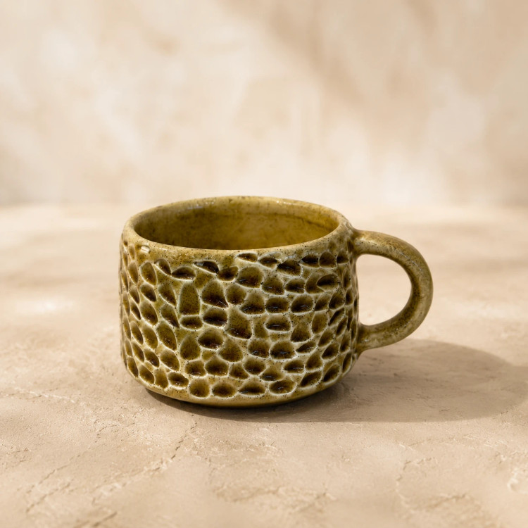 Close-up of a short rounded ceramic cup with glossy olive glaze and raised hand-carved pattern