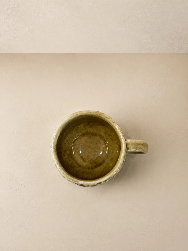 Close-up of a short rounded ceramic cup with glossy olive glaze and raised hand-carved pattern