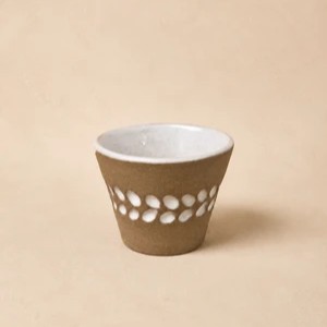 نمایش نزدیک از نقوش ارگانیک و برجسته شبیه دانه یا برگ با جزئیات لعاب سفید روی فنجان بدون دسته.